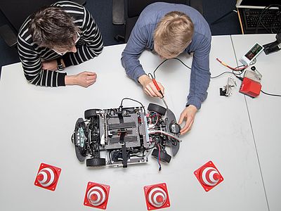 Zwei Personen arbeiten an einem selbstfahrenden Modellauto.