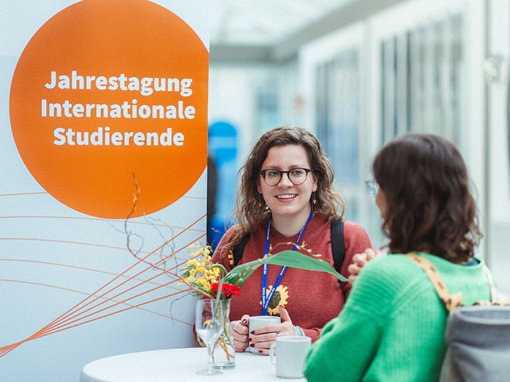 DAAD Tagung 2024 Slider Auf der Illustration ist ein Bild von der DAAD Tagung eingebetet mit den Corporate Design
