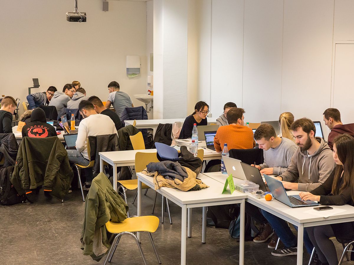 Studierende sitzen in Gruppen zusammen und arbeiten an Laptops