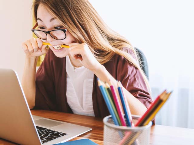 Frau sitzt vor Notebook und beisst in einen Buntstift.